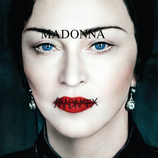 Close-up portrait of Madonna with the word 'MADONNA' across her forehead and 'MADAMEX' crossed out in black ink on her lips. She has bright blue eyes, pale skin, red lipstick, dangling earrings, and a dark collar against a dark teal background.