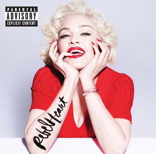 Madonna wearing a red top with 'Rebel Heart' tattoo on arm, against a plain background.